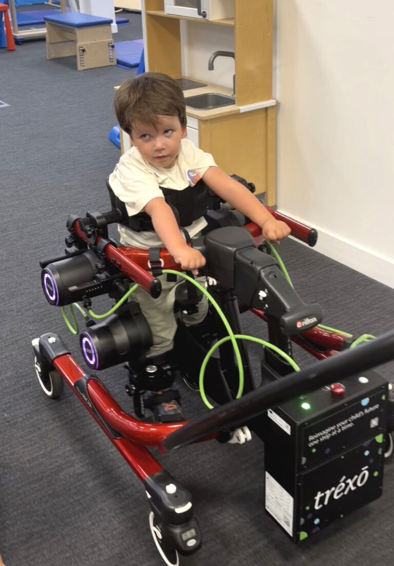 Adriaan loopt met een staprobot, een rode rollator met motoren aan de benen, in een therapiezaal