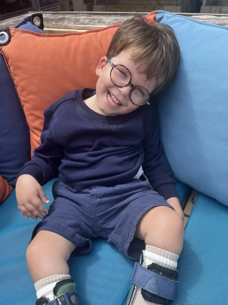 Adriaan lacht met zijn nieuwe bril op, zittend tussen blauwe en oranje kussens op een zetel
