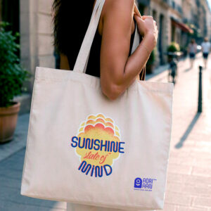 katoenen draagtas met “Sunshine state of mind” print en klein ADRIAAN vzw logo, gedragen over de schouder in een winkelstraat