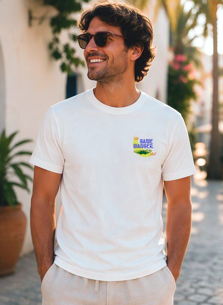 Wit T-shirt met klein “The Game Changer club” logo op de linker borst, gedragen door een lachende man in een zonnige straat