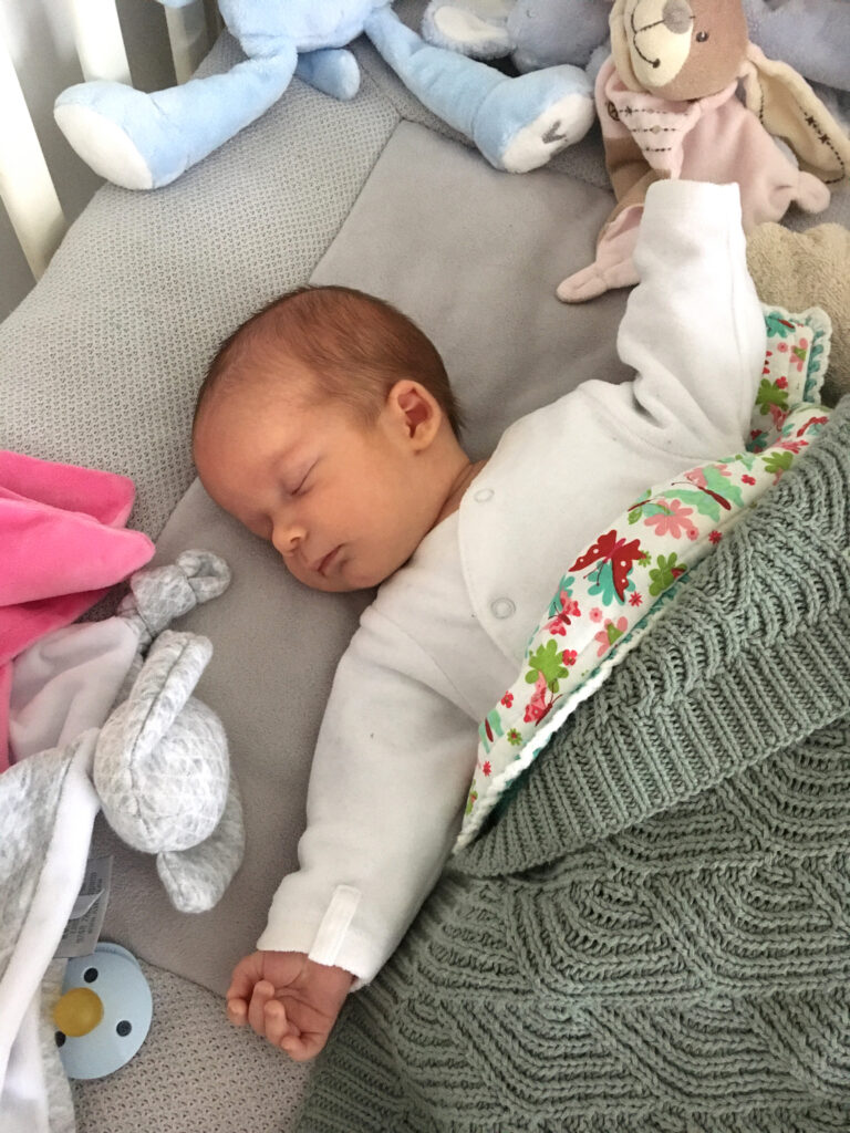 Slapende pasgeboren Adriaan in zijn bedje tussen zijn knuffels